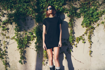 stylish young woman dressed on a black blank t-shirt posing on a background of a concrete wall with...