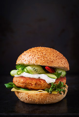 Big sandwich - hamburger with juicy chicken burger, cheese, cucumber, chili and tartar sauce on black background