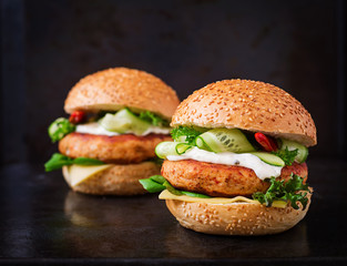 Big sandwich - hamburger with juicy chicken burger, cheese, cucumber, chili and tartar sauce on black background