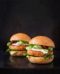 Big sandwich - hamburger with juicy chicken burger, cheese, cucumber, chili and tartar sauce on black background
