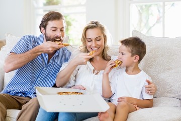 Parents and child sitting on sofa and having pizza