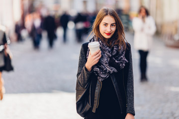 Fototapeta premium Young girl walking on the street with cup of hot coffee