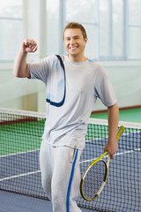 young man smiling and posing with tennis racket indoor