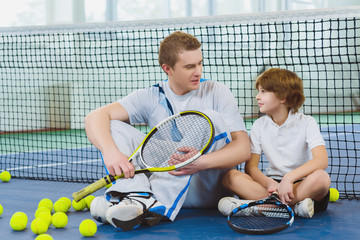 Resting young man or tennis coach with boy sitting near net