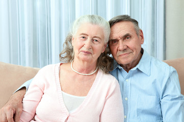 Affectionate elderly couple with beautiful beaming friendly smiles posing together in a close embrace in their living room. Portrait of a candid senior couple enjoying their retirement.