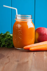 Healthy carrot apple smoothie in a jar on blue wooden background