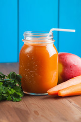Healthy carrot apple smoothie in a jar on blue wooden background
