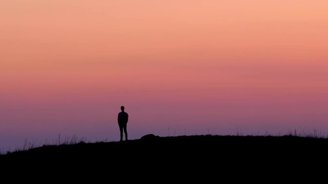 A young man is standing on top of a hill / mountain right after sunset. He is looking out over the amazing view and has a feeling of accomplishment and freedom. Filmed in 4k UHD high resolution.
