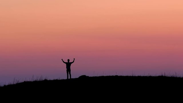A young man is standing on top of a hill / mountain and raises his arms gesturing a feeling of winning and success. Shot in 4k UHD high resolution.
