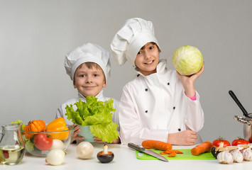two smiling children-cooks by the table with vegetables
