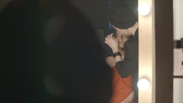 Male makeup artist applying primer on eyelids of a model with sponge in front of mirror with lights