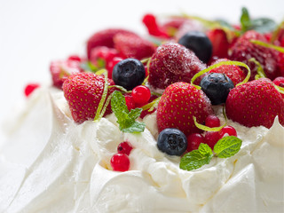 Meringue cake Pavlova with whipped cream, frozen strawberries, blueberries  and red currants