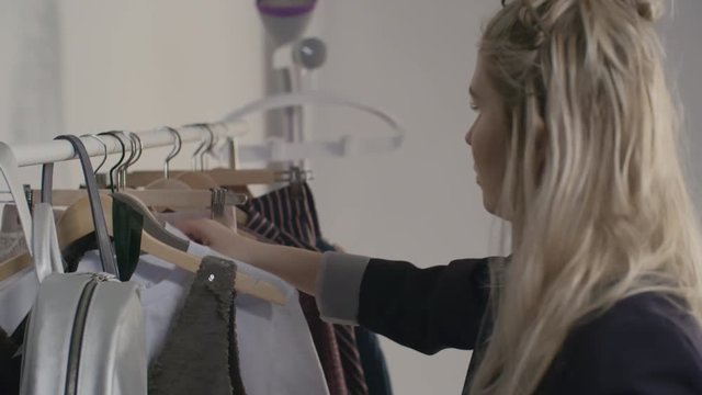 Stylist browsing through clothes on rack and choosing white shirt 