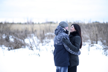 Fototapeta na wymiar Happy young couple hugging outdoors in a snowy park. Love hugs, family relationships