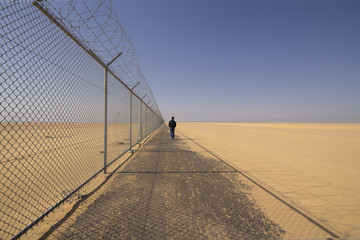 A man walking in the side way next to the border fence - 107947846