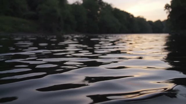 Closeup of river water at sunset in slow motion. Insects interact with the river ripples on a warm summers evening