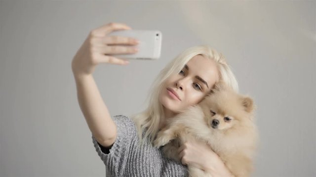 Beautiful Blonde Woman Making Selfie With Her Spitz Isolated On Grey