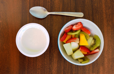 Bowl with tropical fruits, some yogurt and a spoon on a black table