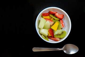 Bowl with tropical fruits and a spoon on a black table