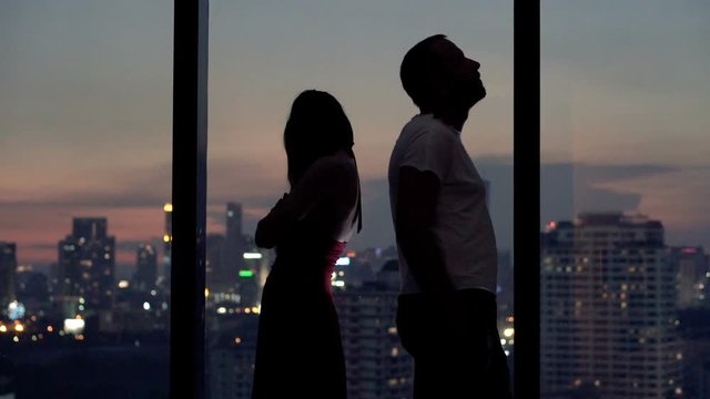 Sad, offended couple standing by window at home at night
