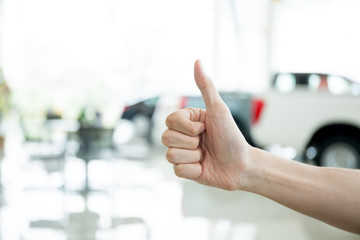 Human hands giving thumbs up with car key in car shoowroom