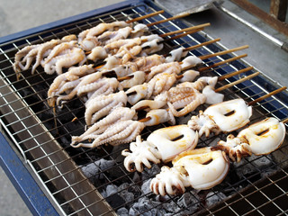 group of fresh white squid skewers grilling on steel grate charcoal stove