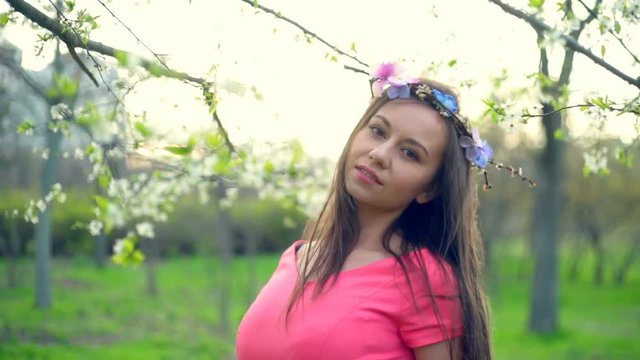 young female wearing circlet of flowers posing in spring blossom slow motion