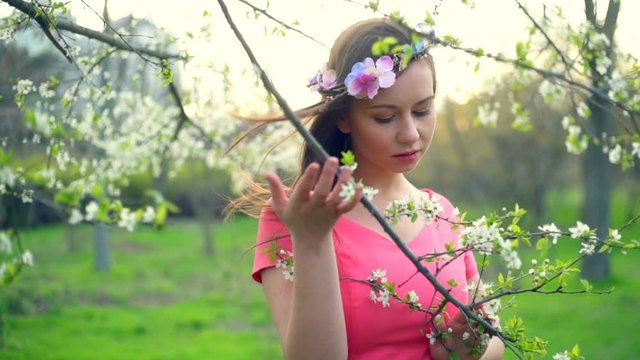 young female wearing circlet of flowers posing in spring blossom slow motion