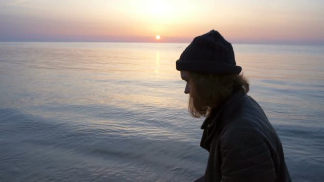 young man holding skateboard walks along the sea shore at the dawn slow motion