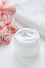 Anti wrinkle anti-aging cosmetic cream face care hygiene moisture lotion with herbal flowers therapy in glass jar with towel on white background