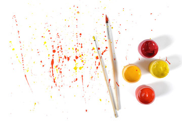 Gouache jars and paint brushes on a white background with colorful spray in top view