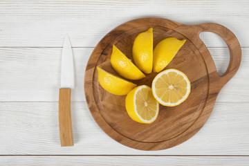 Sliced and whole lemons on cutting board with a knife next to it in top view
