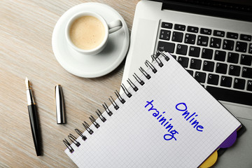 Online training written in the notebook, laptop and cup of coffee on table, top view