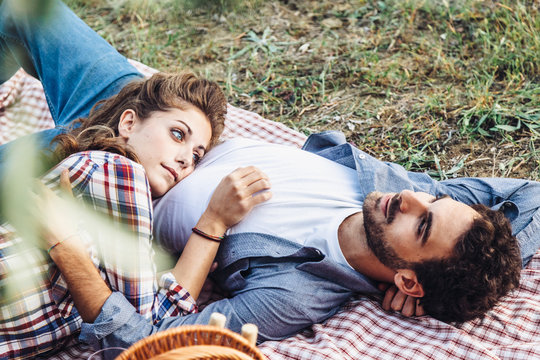 On a late summer day, a pair of young lovers is lying on the grass. The head of the young woman's belly on him. Picture taken in a field in Tuscany, Italy