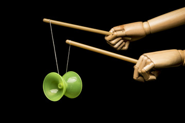 Two wooden hands playing diabolo. Isolated on black background.