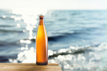 Bottle of cold fresh beer on table, on sea or ocean background