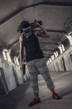 A man in a mask holds gun and skateboard.