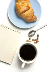 Coffee, croissant and notepad, shot from above on white
