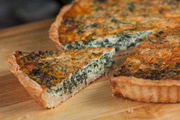 pie with cottage cheese, herbs and cheese with cut pieces on a wooden board