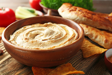 Wooden bowl of tasty hummus with chips and flat bread on table