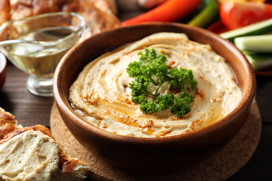 Wooden bowl of tasty hummus with parsley on table, close up