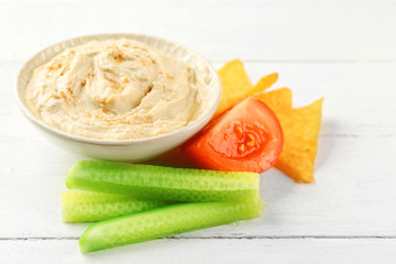 Ceramic bowl of tasty hummus with chips and vegetables on table