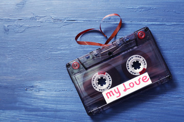Retro audio cassette with tape in shape of heart on wooden background