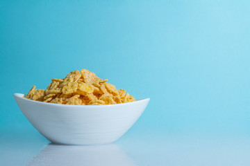 yellow flakes in white plate cup on a light blue sky background close-up
