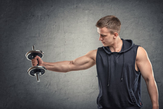 Portrait of muscular young man lifting a dumbbell for training his biceps