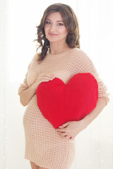 Pregnant woman is holding red heart