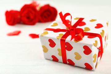 Gift box, rose flowers and decorative hearts on light wooden background