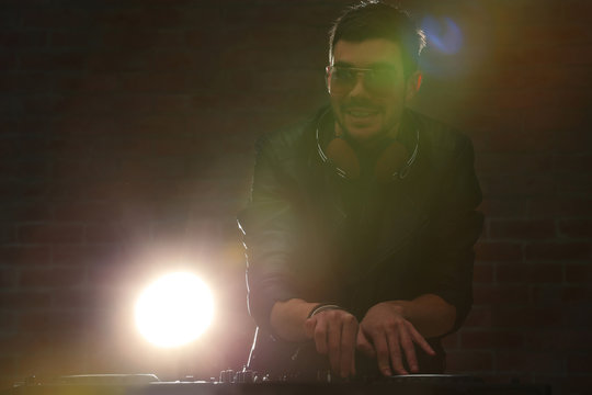 DJ playing music at mixer on blurred brick wall background
