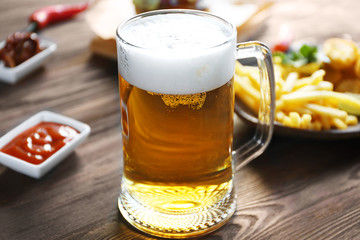 Glass mug of light beer with French fries on dark wooden table, close up