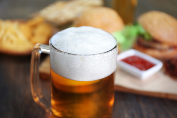Glass mug of light beer with snacks on dark wooden table, close up